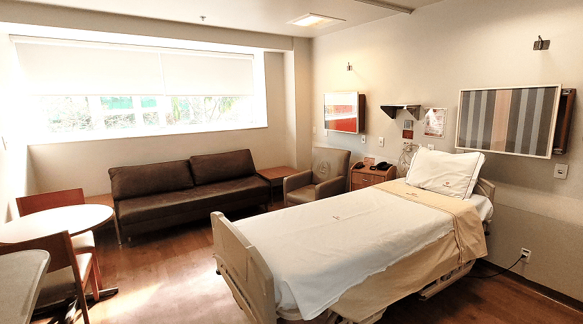 Sala de internação da Perinatal, com uma cama, janela ampla e um sofá de acompanhante