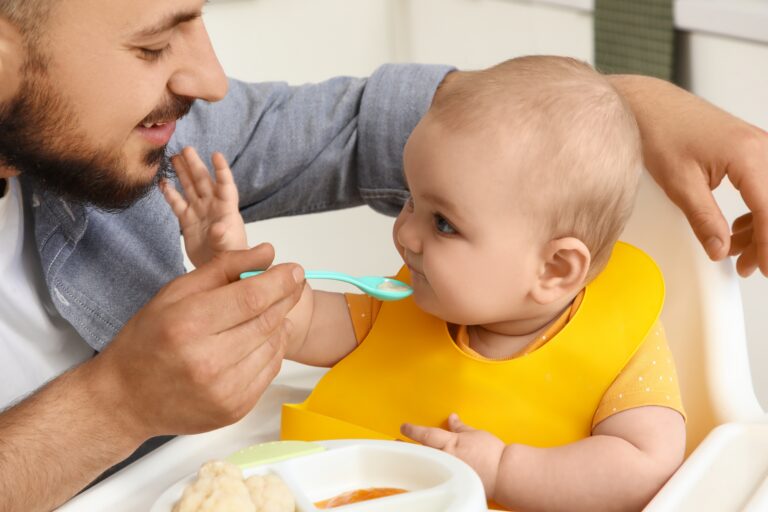 Father,Feeding,His,Little,Baby,In,High,Chair,At,Home,